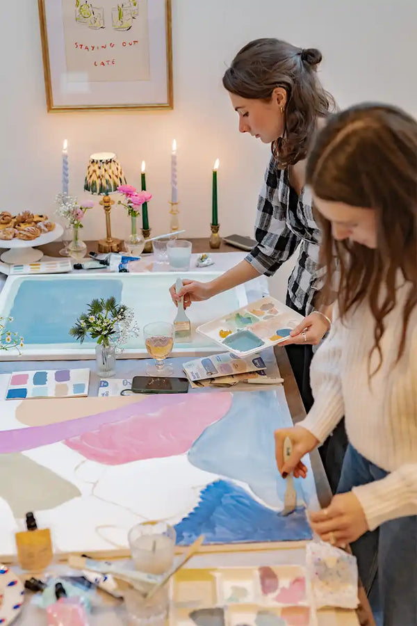 Two women at a table with art supplies and a painting from Sculpd canvas kit